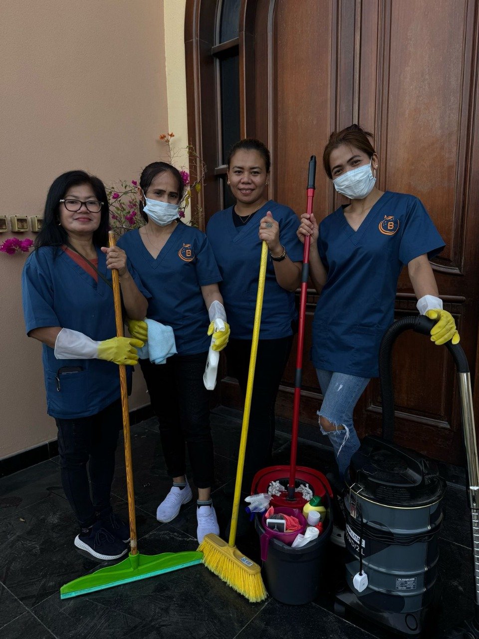 Four female cleaners standing together holding mops